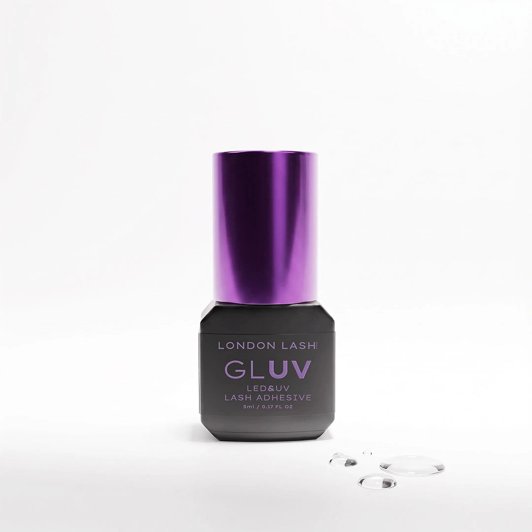 A bottle of London Lash Gluv LED & UV Lash Adhesive with a metallic purple cap and a dark gray/black base, shown on a clean white background with a few clear adhesive drops in the foreground.