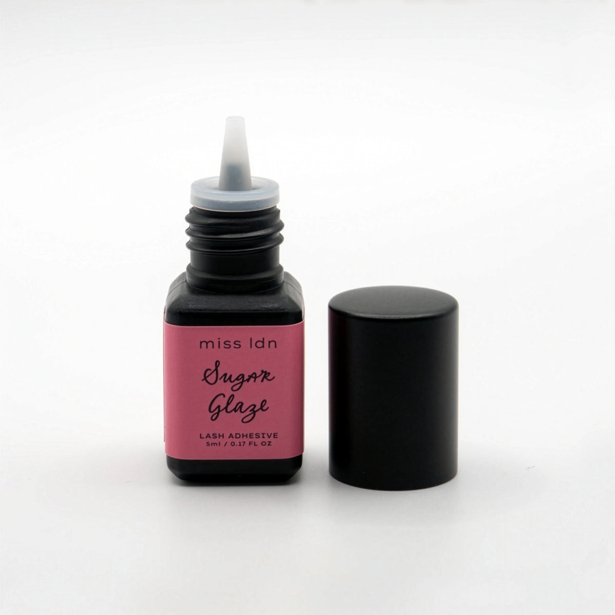 Open bottle of miss idn Sugar Glaze lash adhesive with pink label on a white background